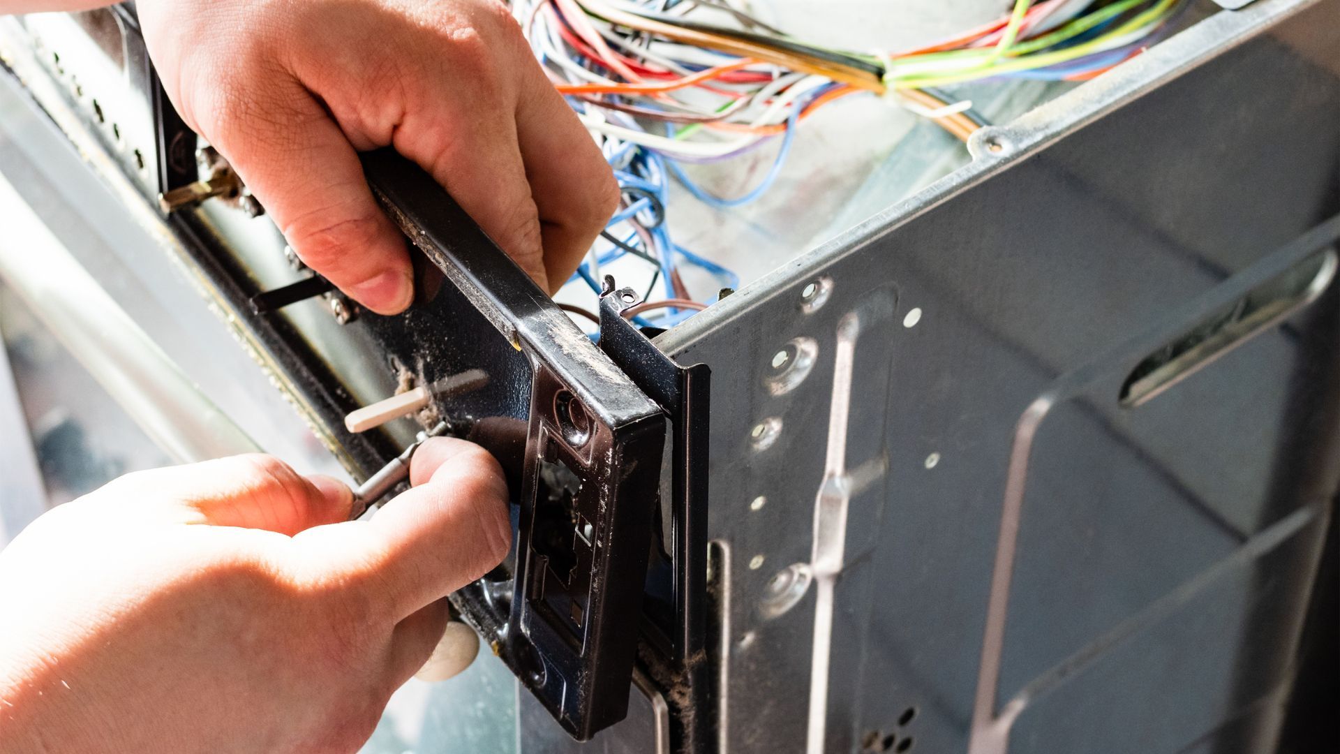 A person is fixing a dishwasher with a screwdriver.