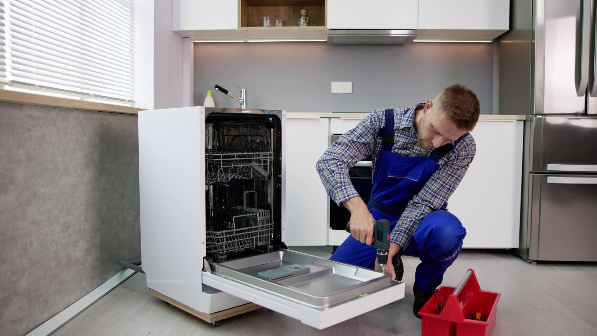 A man is fixing a dishwasher in a kitchen.