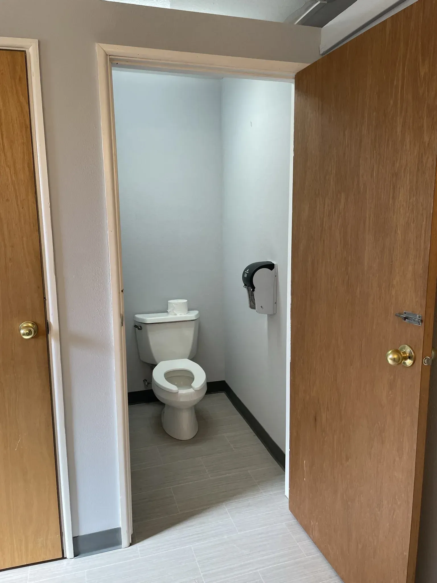 A doorway opens to a small restroom with a toilet, paper towel dispenser, and neutral-colored walls.