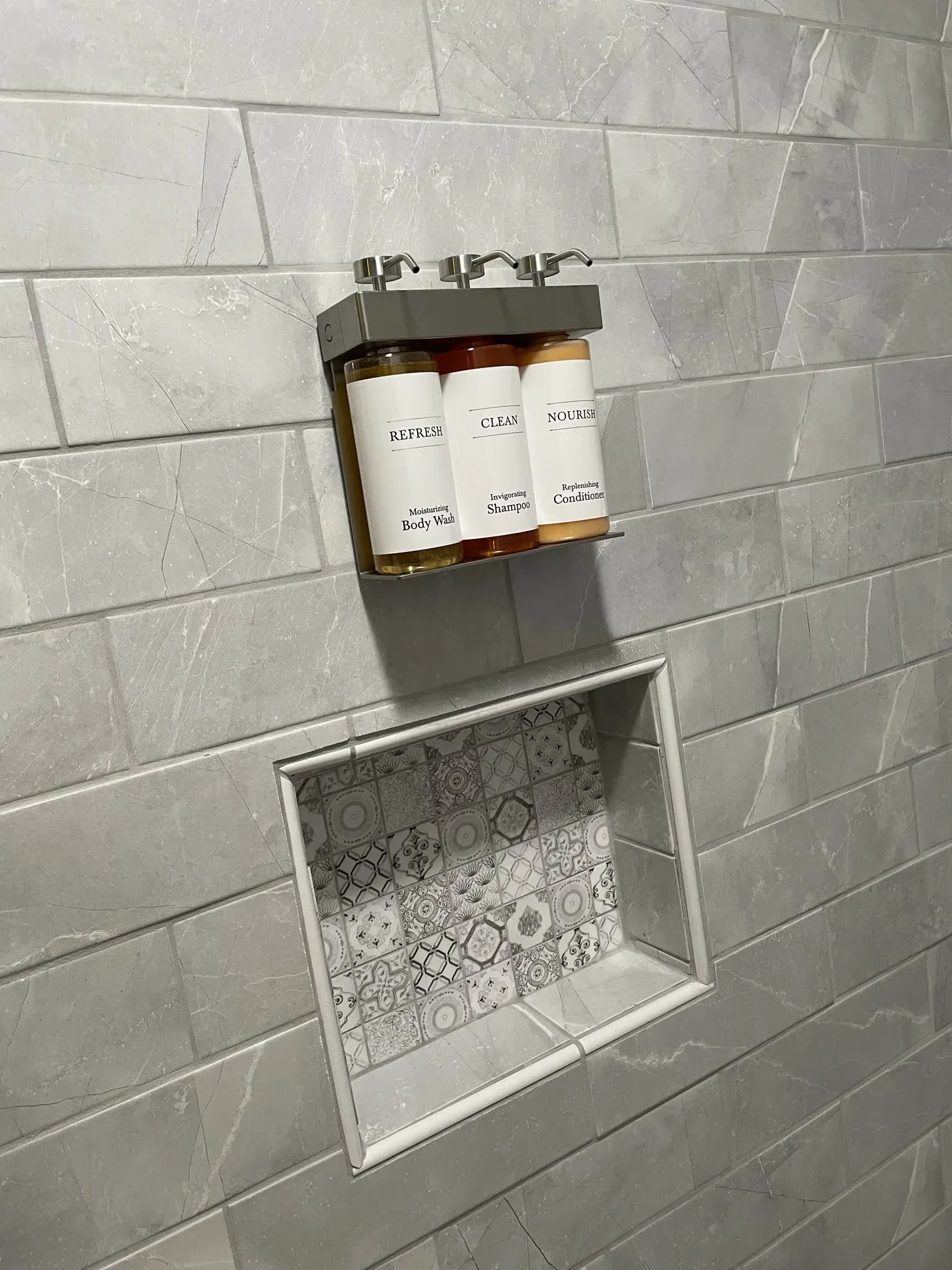 Gray tiled shower wall with shampoo bottles and a recessed shelf.