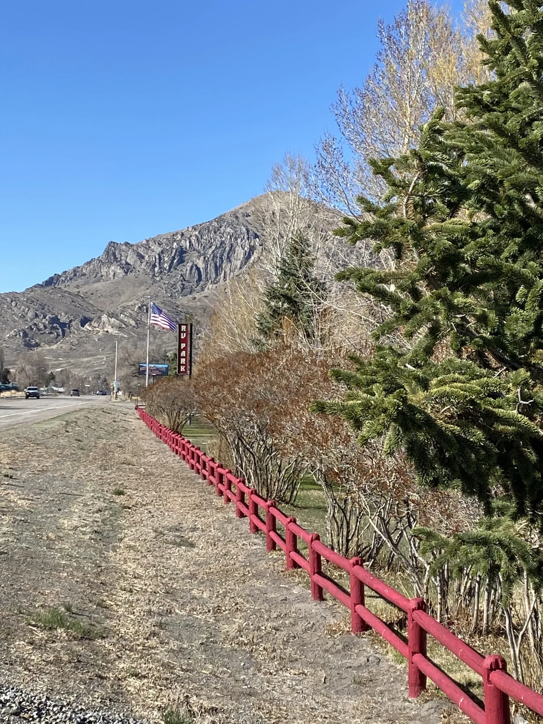 Red fence along a road with a mountain in the background under a blue sky.