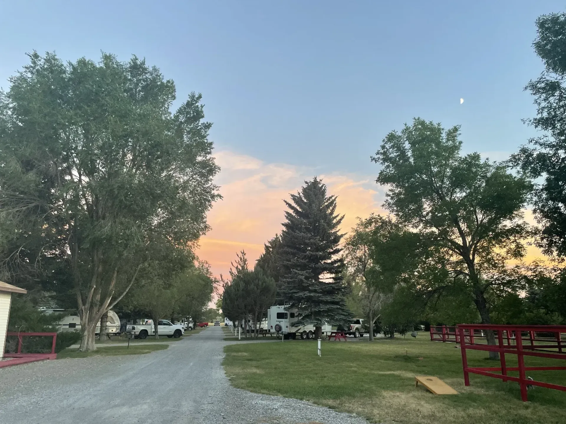Campsite at dusk with a gravel road, RVs, trees, and colorful sky.
