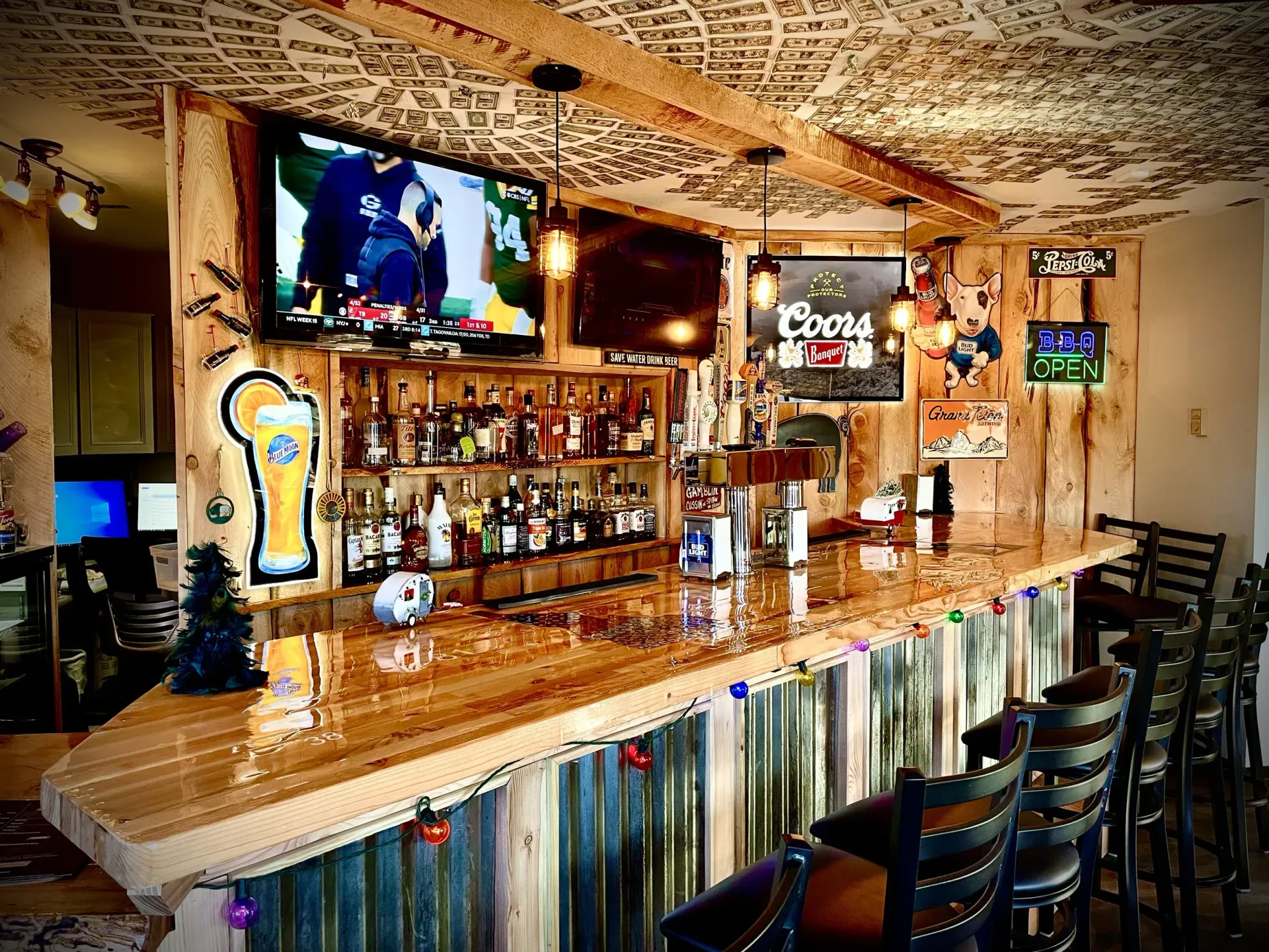 Bar with wooden counter and liquor bottles, TV screens, and hanging lights.