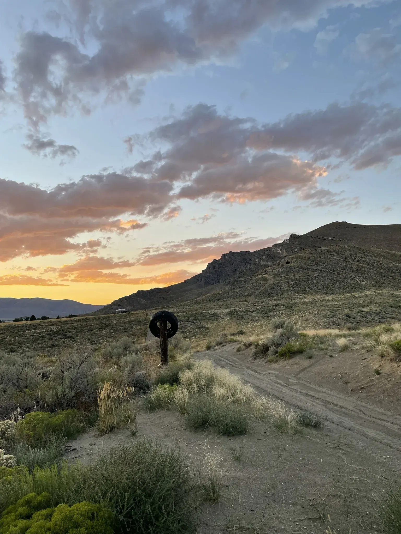 Dirt path through desert landscape towards a rocky hill, sunset colors in the sky.