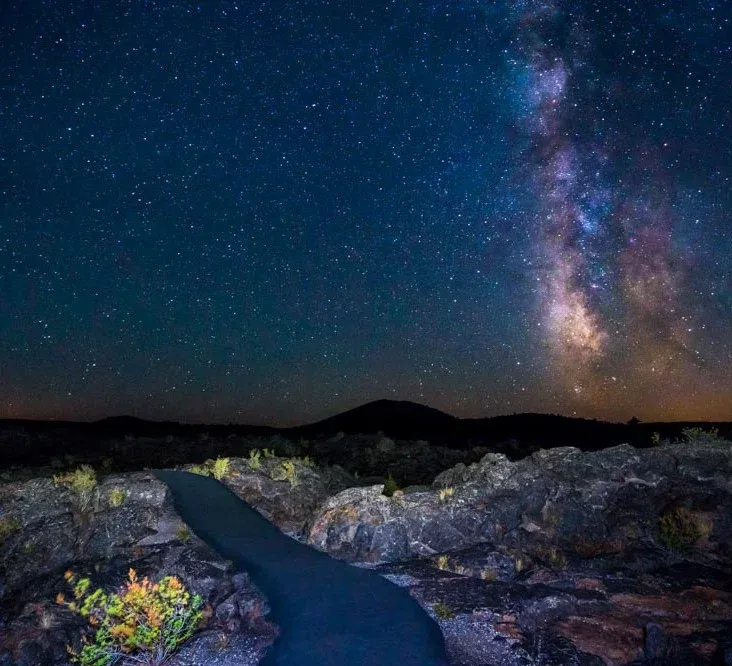 Dark night sky with the Milky Way above a paved path winding through a rocky landscape.