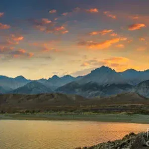 Mountains under a colorful sunset sky reflected in calm water.