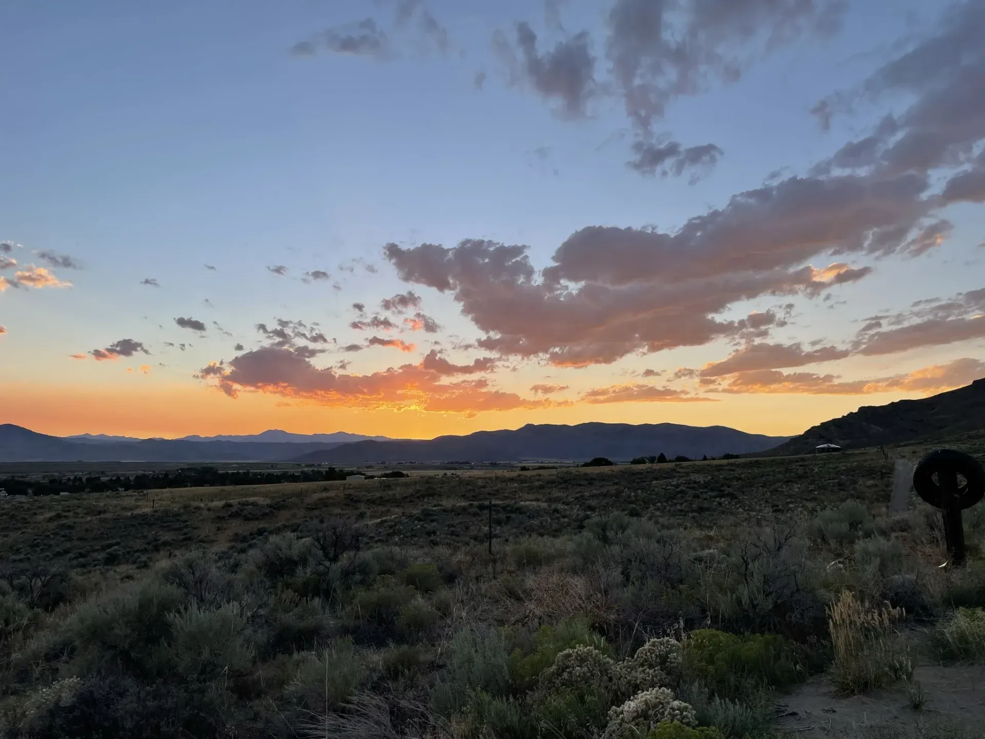 Sunset over desert landscape with orange, yellow, and blue sky; low brush in foreground.