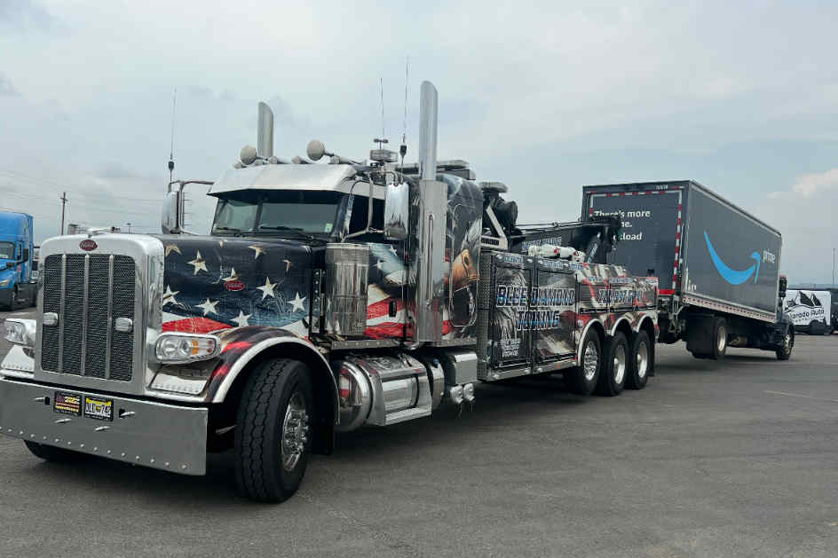 Peterbilt tow truck with American flag design pulling an Amazon trailer.