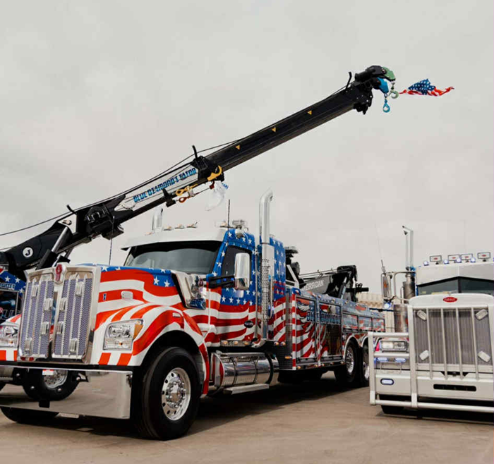 Tow truck with patriotic American flag design, extended crane, parked outside.