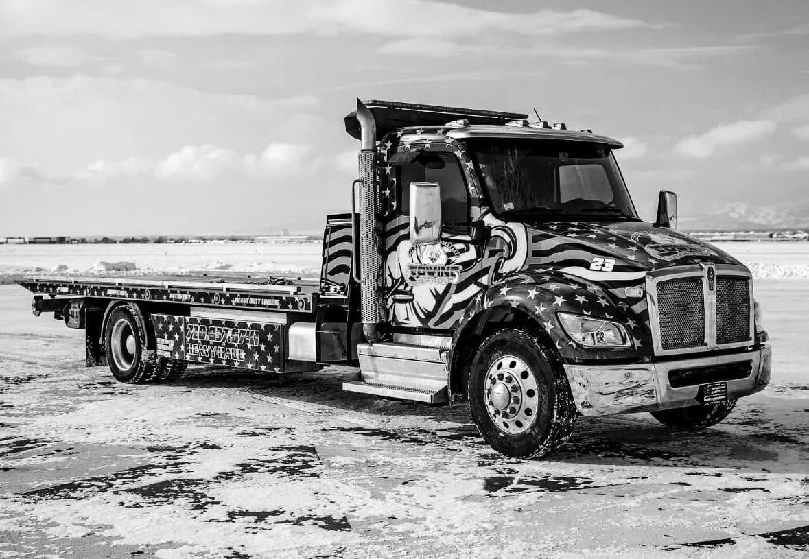 Black and white tow truck with American flag design on snowy ground.