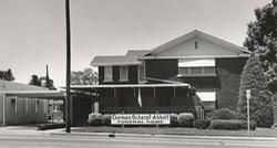 German Scharl Abbott Funeral Home in black and white. Building with sign and shrubs.