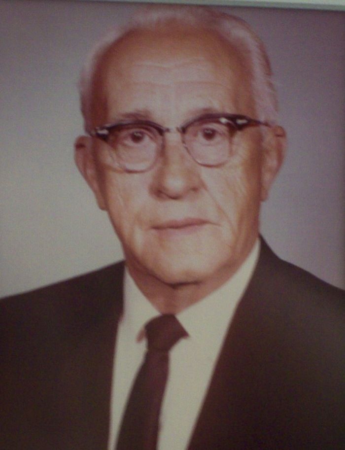 Formal portrait of an older man in glasses and suit, looking at the viewer.