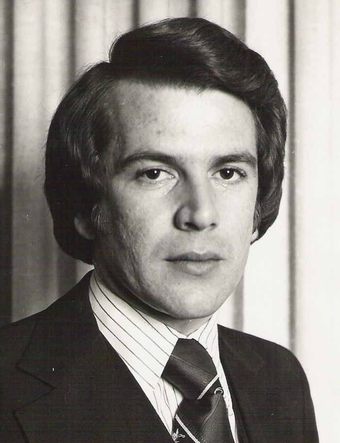 Man in suit and tie with brown hair, looking at the camera. Studio setting, striped tie.