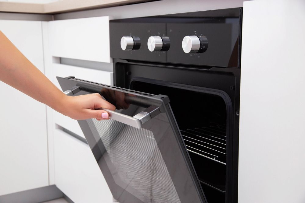 A Person is Opening the Door of an Oven in a Kitchen — Garrow's TV & Antenna Services in Caloundra West, QLD