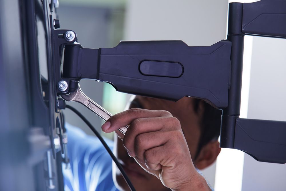 A Man is Fixing a Tv Mount With a Wrench — Garrow's TV & Antenna Services in Caloundra West, QLD