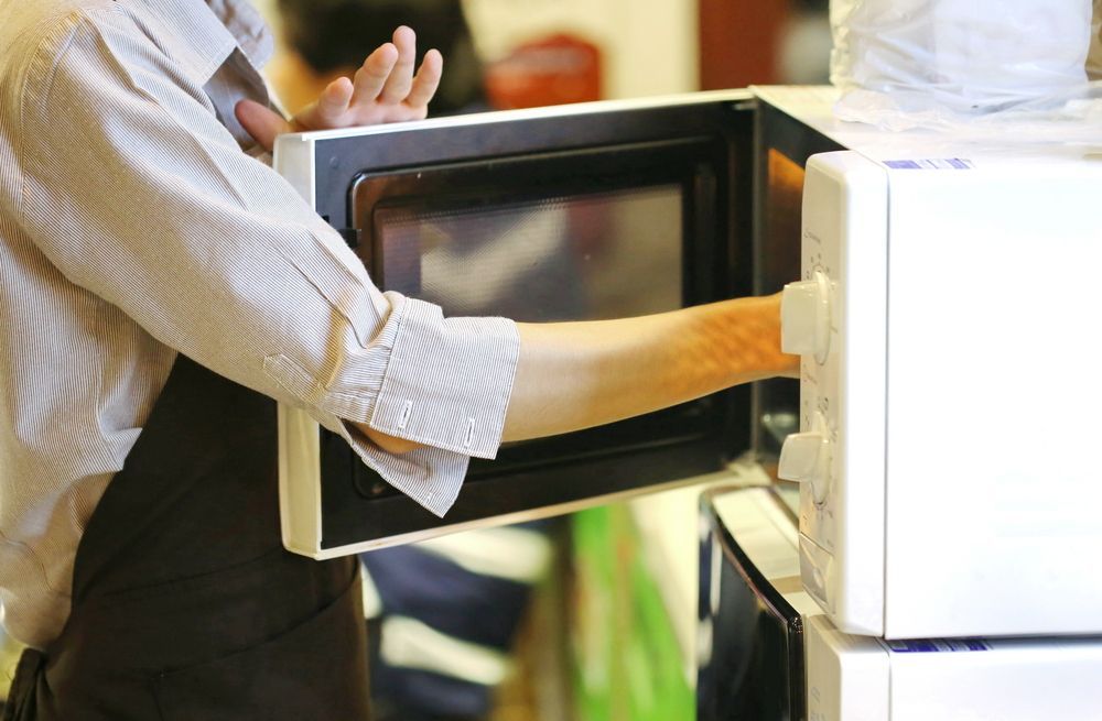 A Man is Taking Something Out of a Microwave Oven — Garrow's TV & Antenna Services in Caloundra West, QLD