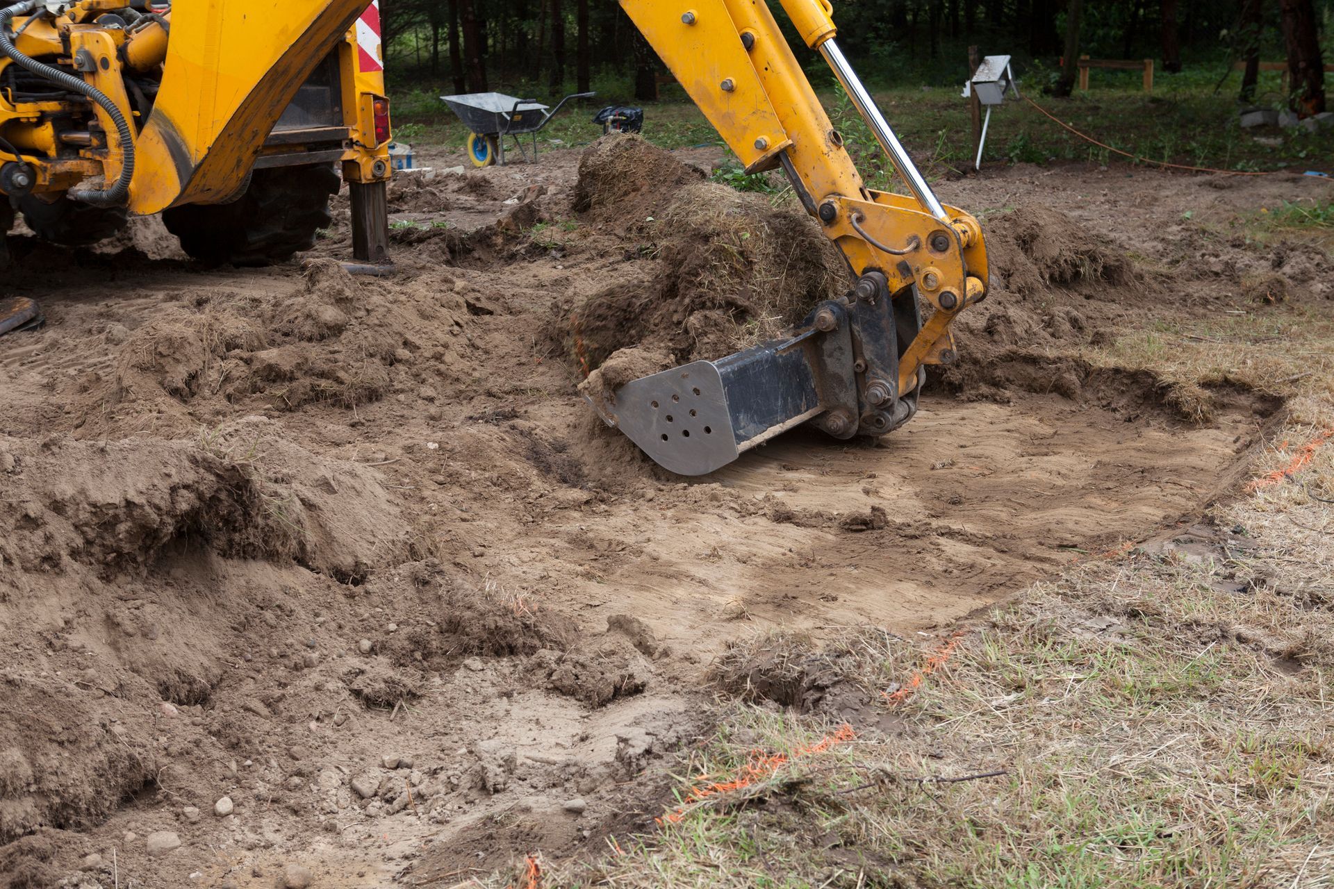 A backhoe excavator digging in muddy earth outdoors. The machine is yellow and the ground is brown.