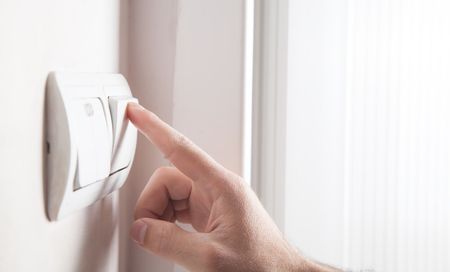 Finger pressing a white wall thermostat on a bright wall