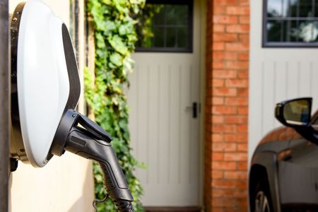 Electric car charging at a home driveway with a black cable plugged in.
