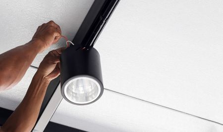 Hands installing a black track light on a white ceiling