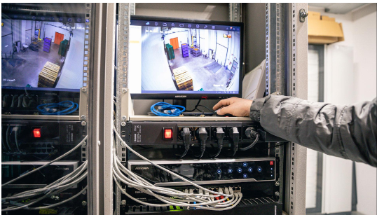 Tecnico che regola le apparecchiature in un rack per server con monitor che mostrano filmati di laboratorio