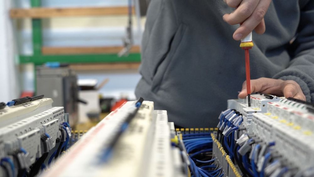 Tecnico che utilizza un cacciavite per lavorare su quadri elettrici con cavi blu in un'officina.