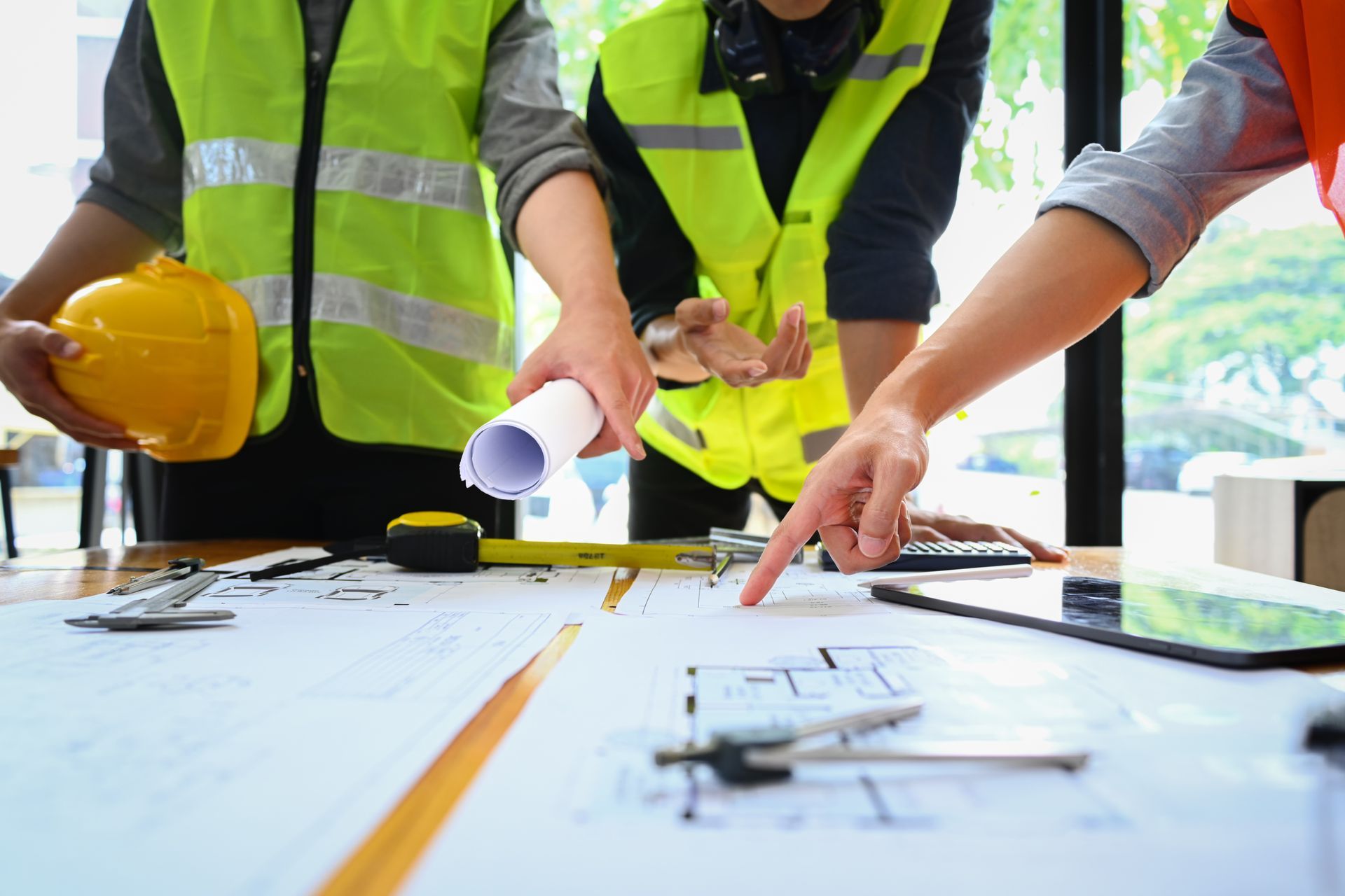 Three engineers in safety vests and hard hats collaborating on a building project at an office.