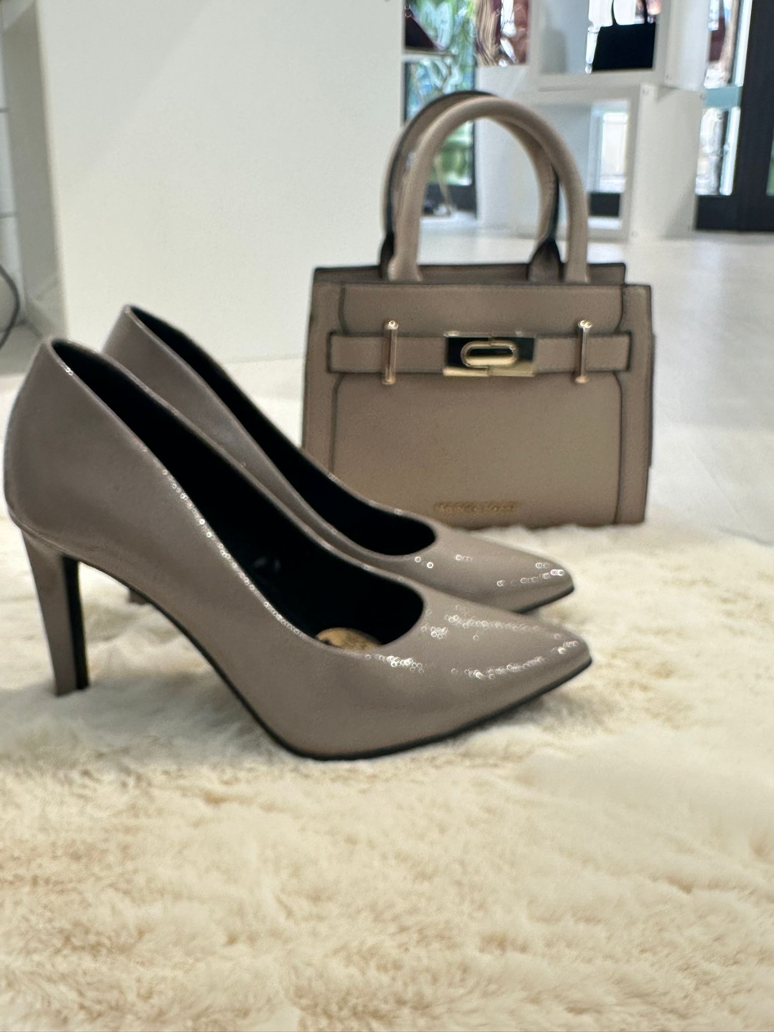 Scarpe con tacco color talpa e borsa coordinata su un soffice tappeto.