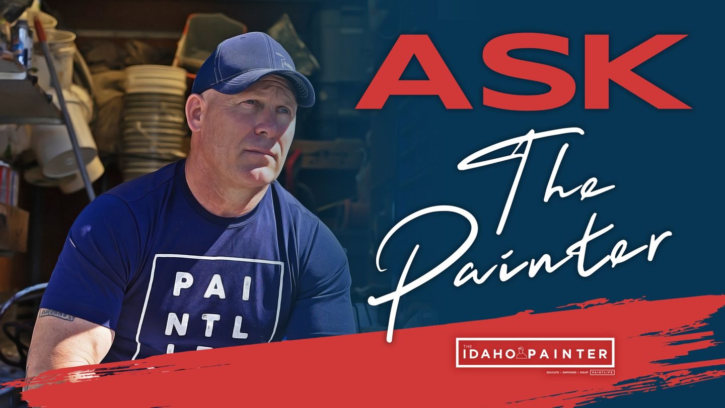 A man wearing a hat and a blue shirt is standing in front of a sign that says ask the painter.