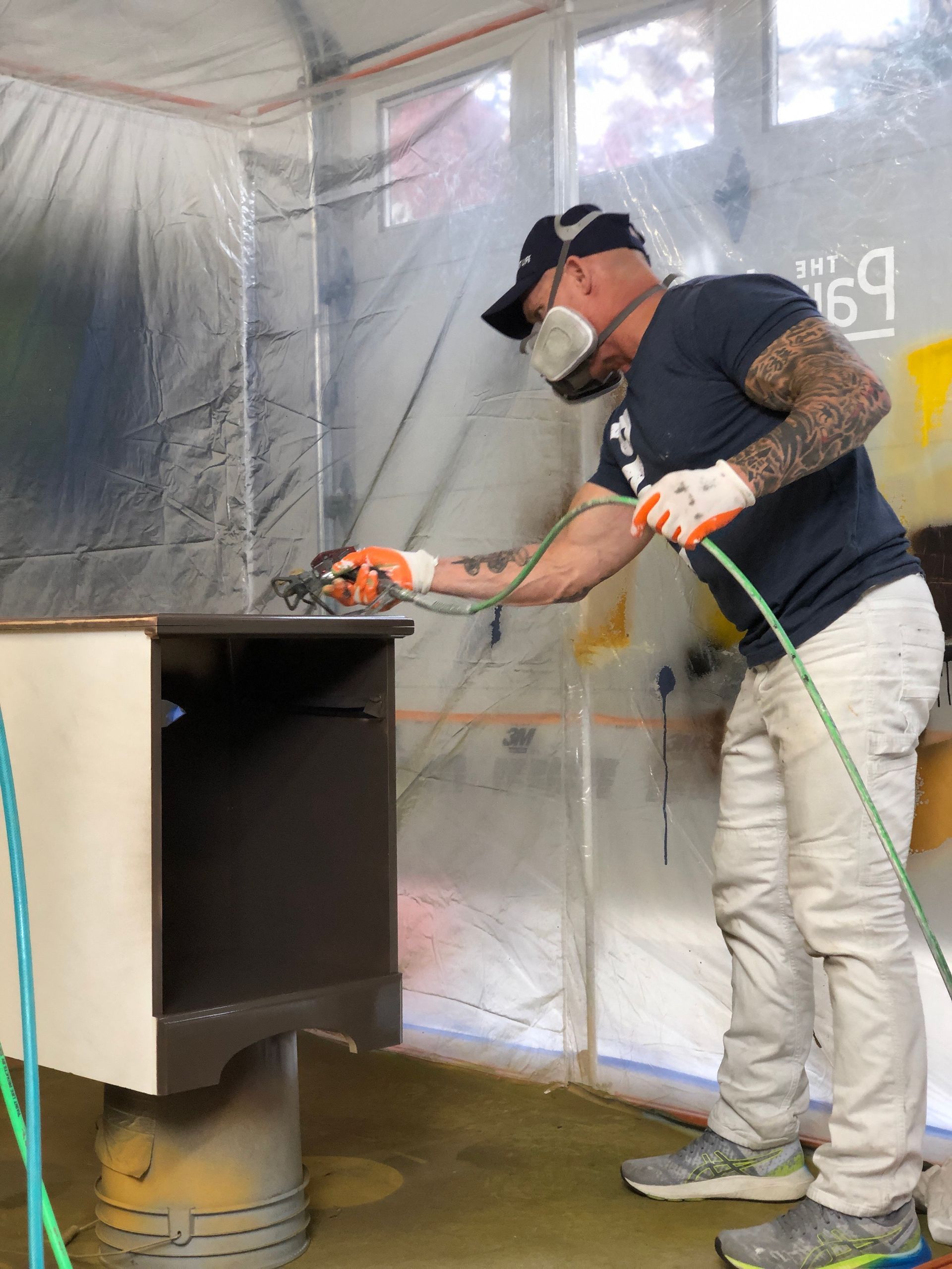 The Idaho Painter wearing a mask is spray painting a cabinet.