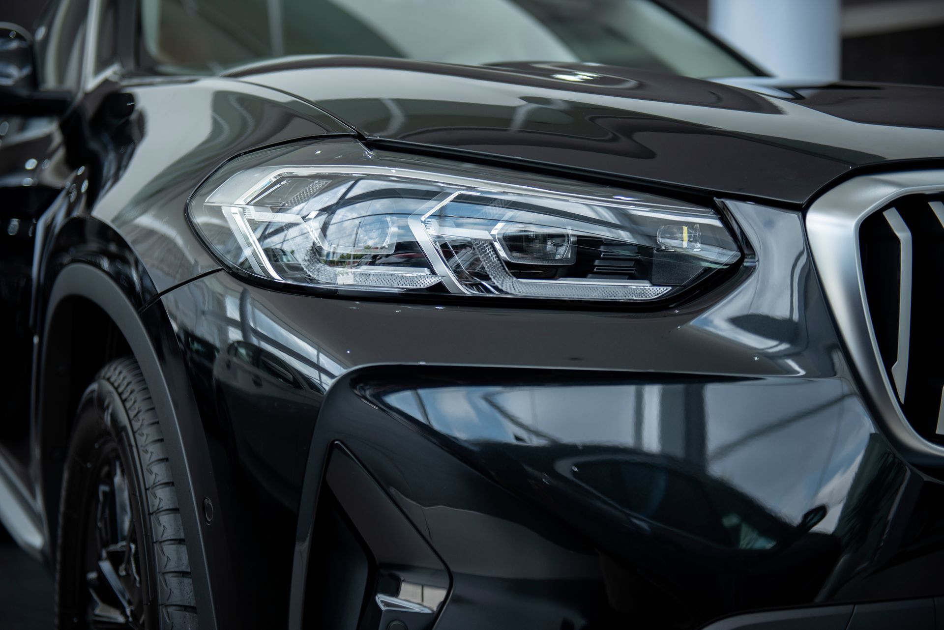 Front view of a black car with a chrome grille and headlight in a showroom