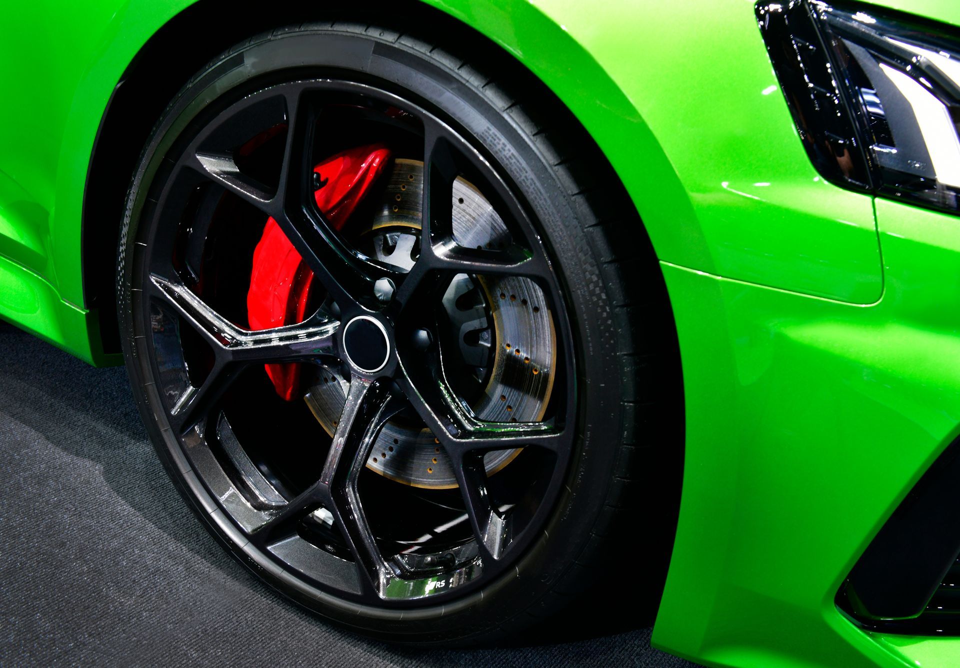 Close-up of a bright green sports car wheel with black rim and red brake caliper