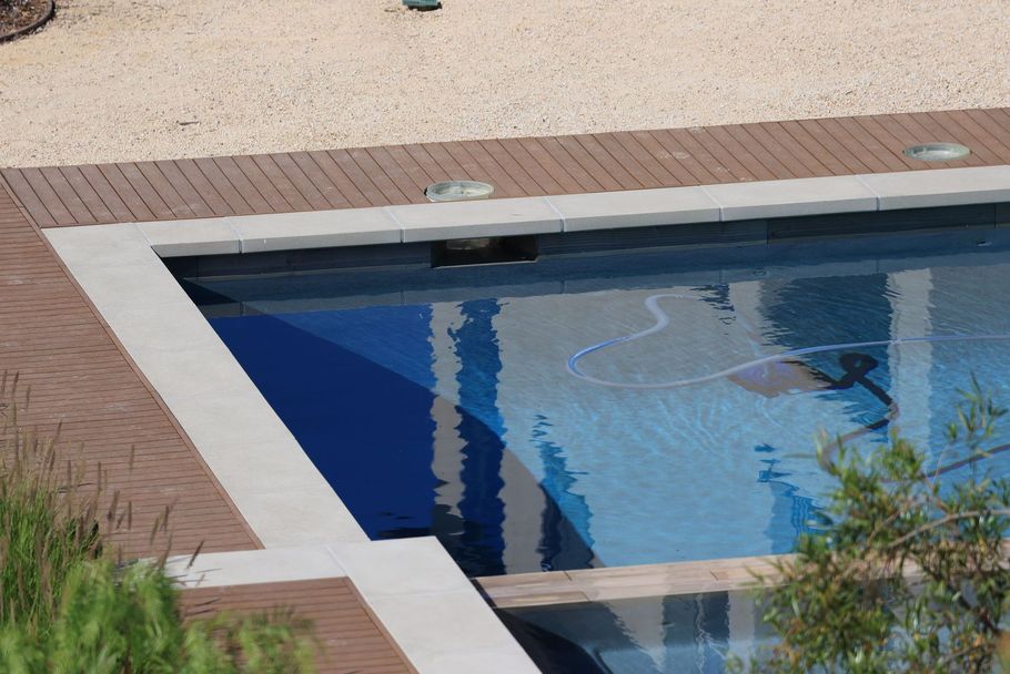 Outdoor swimming pool with blue water, white coping, and tan pool deck.