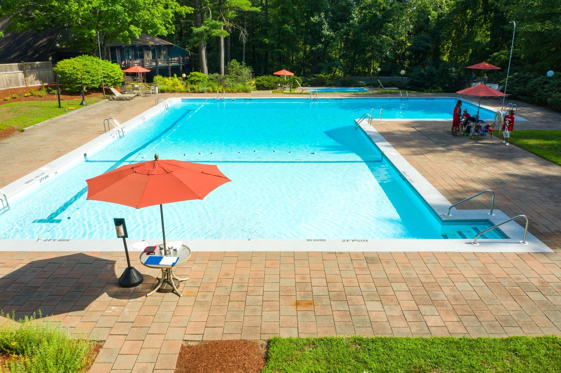 Outdoor swimming pool with a bright blue shallow area, orange umbrellas, lounge chairs, and trees in the background