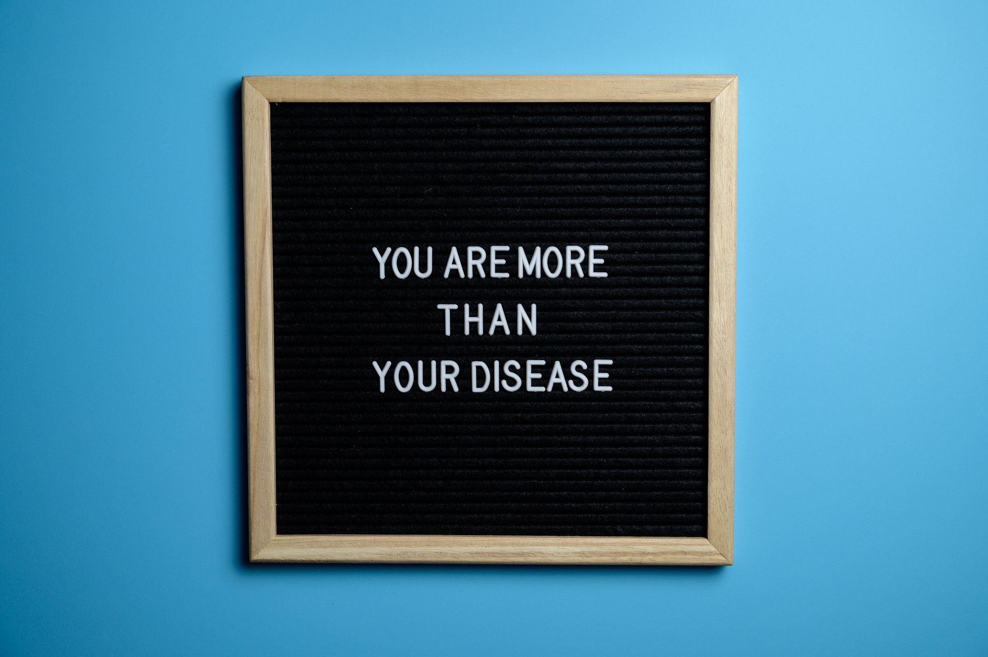 Framed letter board on blue wall reading “YOU ARE MORE THAN YOUR DISEASE”