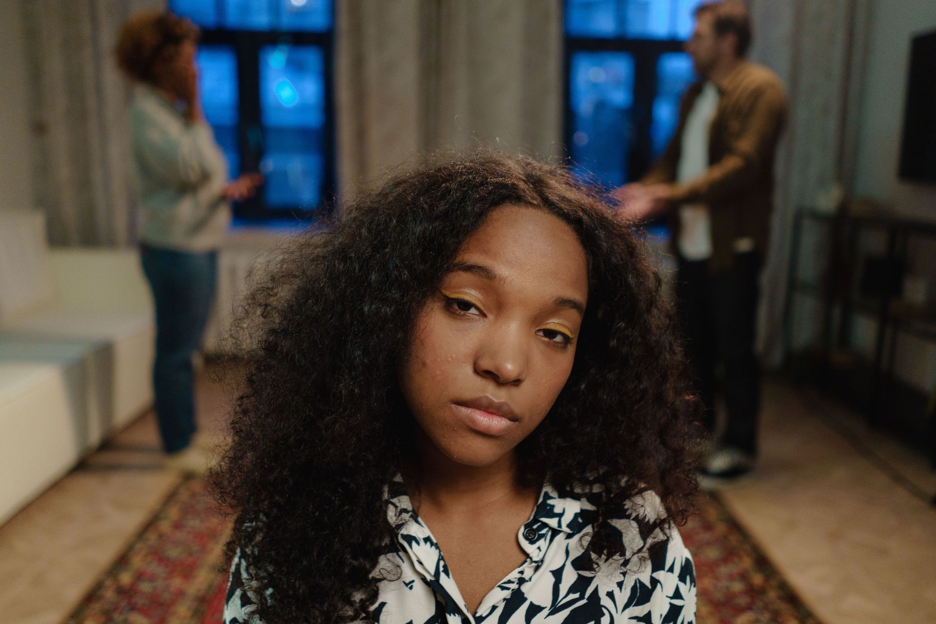 Portrait of a woman with curly hair in a hallway, looking at the camera, with two people blurred in the background