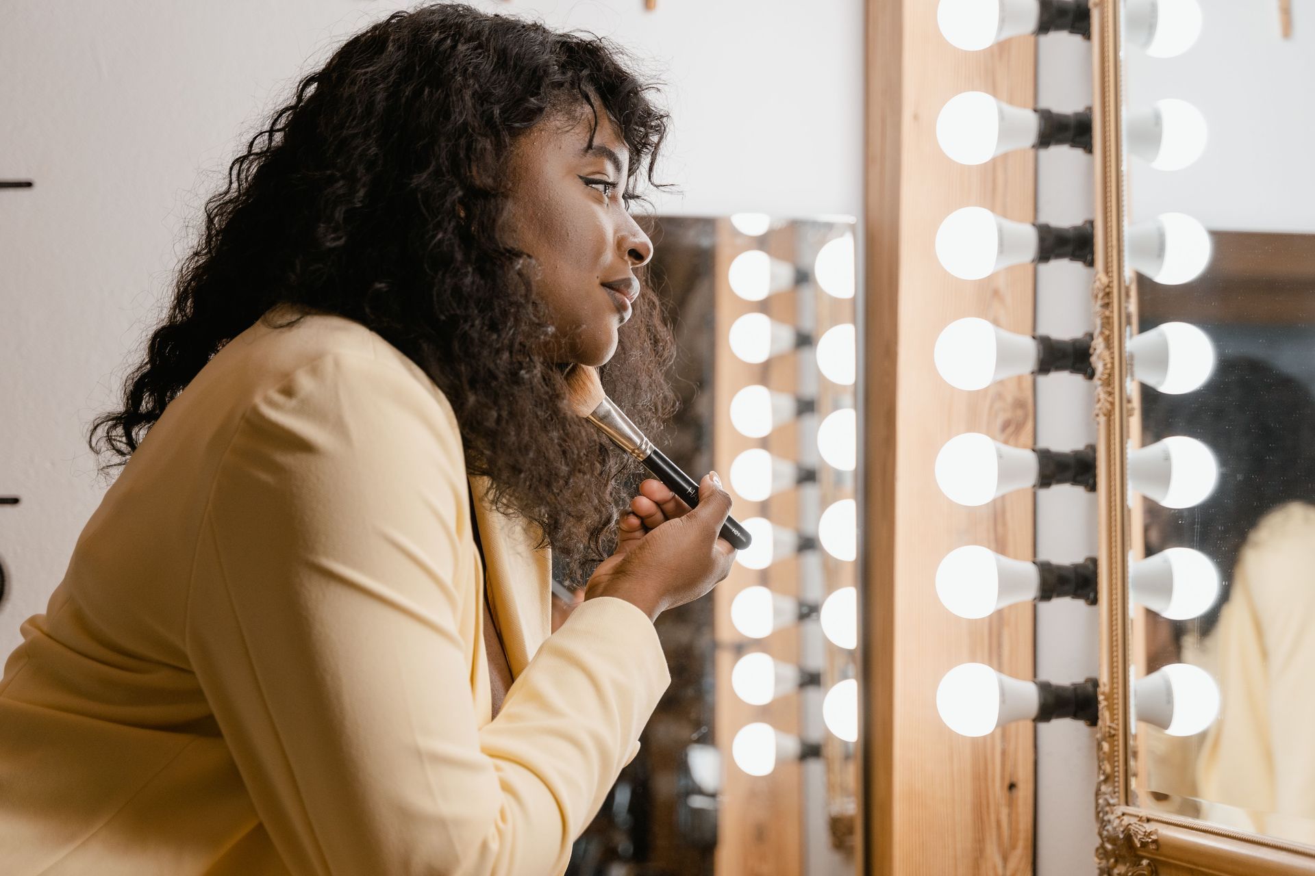 Person applying makeup at a vanity mirror with bright round lights