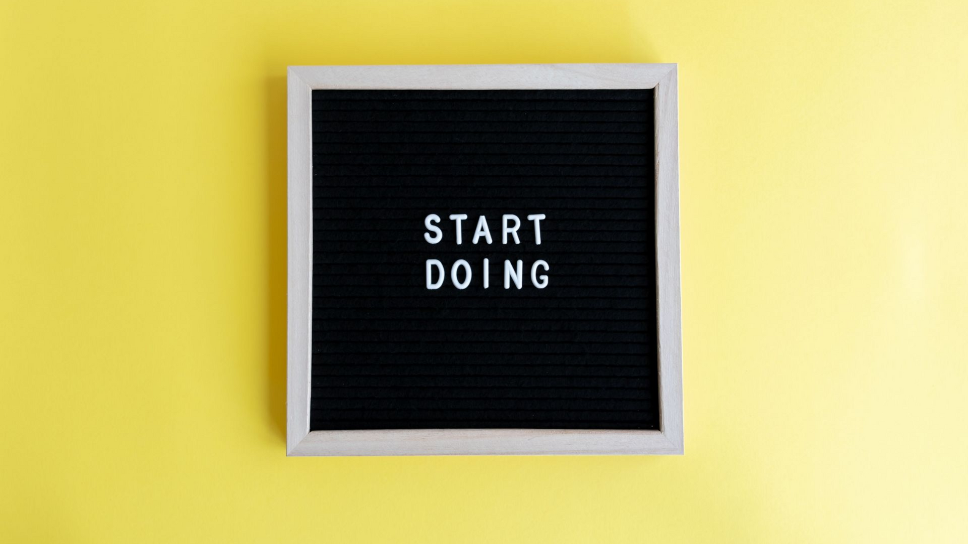 Black letter board on a yellow wall reading “START DOING”