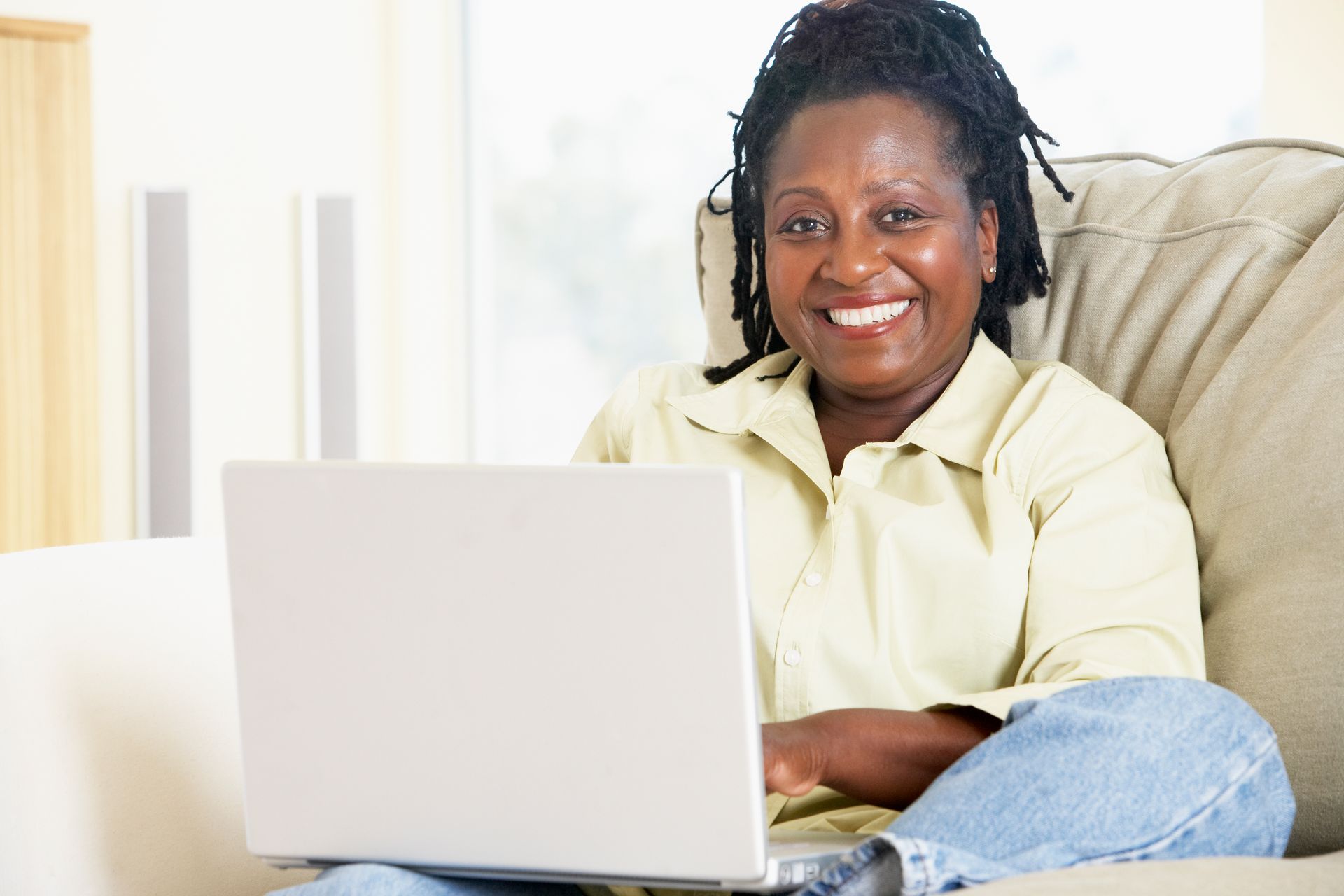 Woman smiling on a couch using a laptop in a bright living room