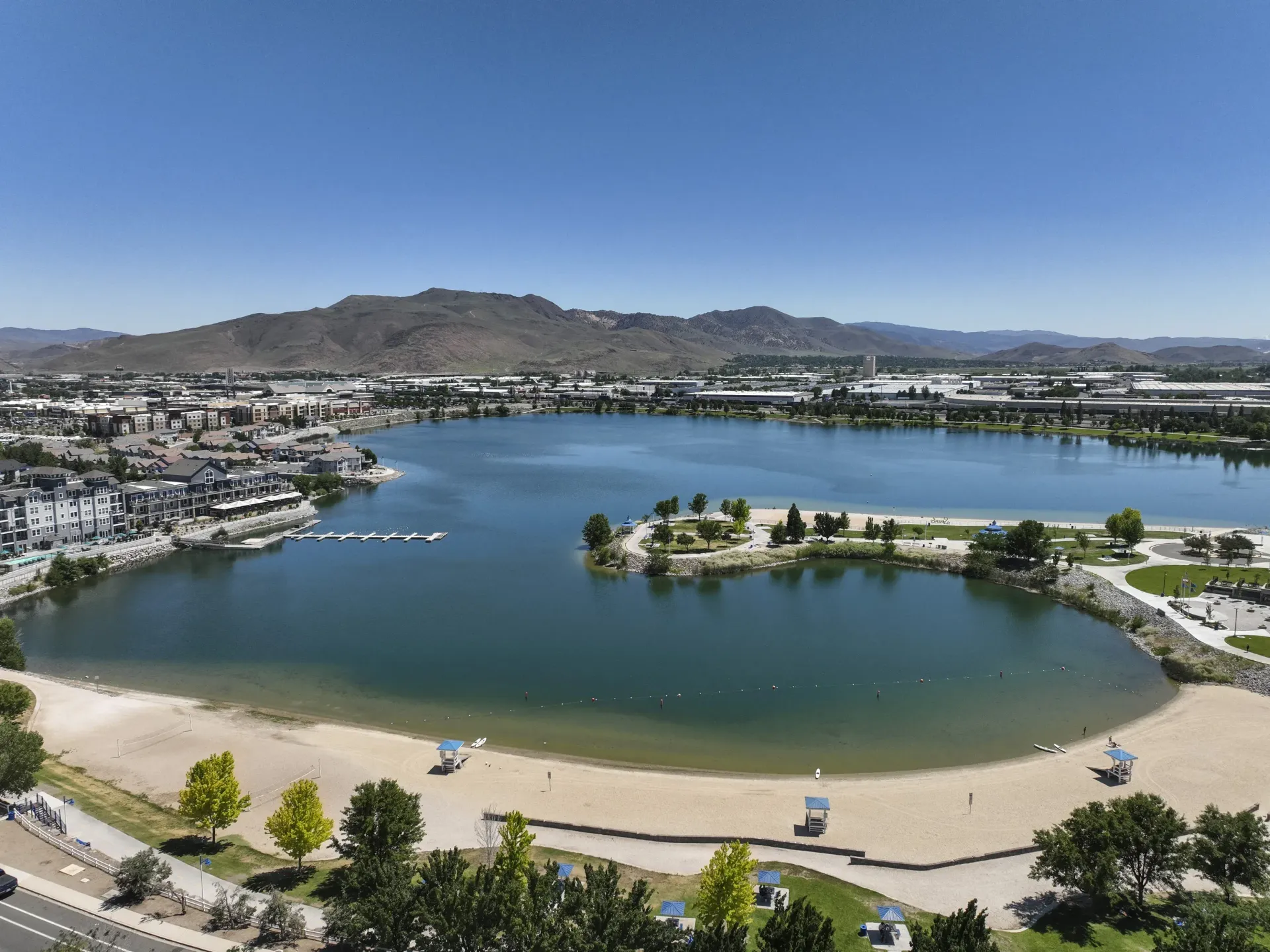 Aerial view of a lake with a park, walking paths, and surrounding apartment buildings at Marina's Edge.