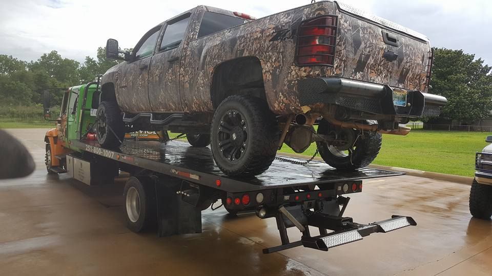 Muddy lifted pickup truck strapped on a flatbed trailer in a wet parking lot