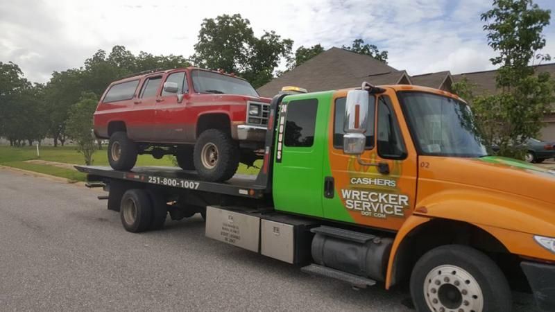 Orange-and-green tow truck hauling a red SUV on a flatbed in a suburban street