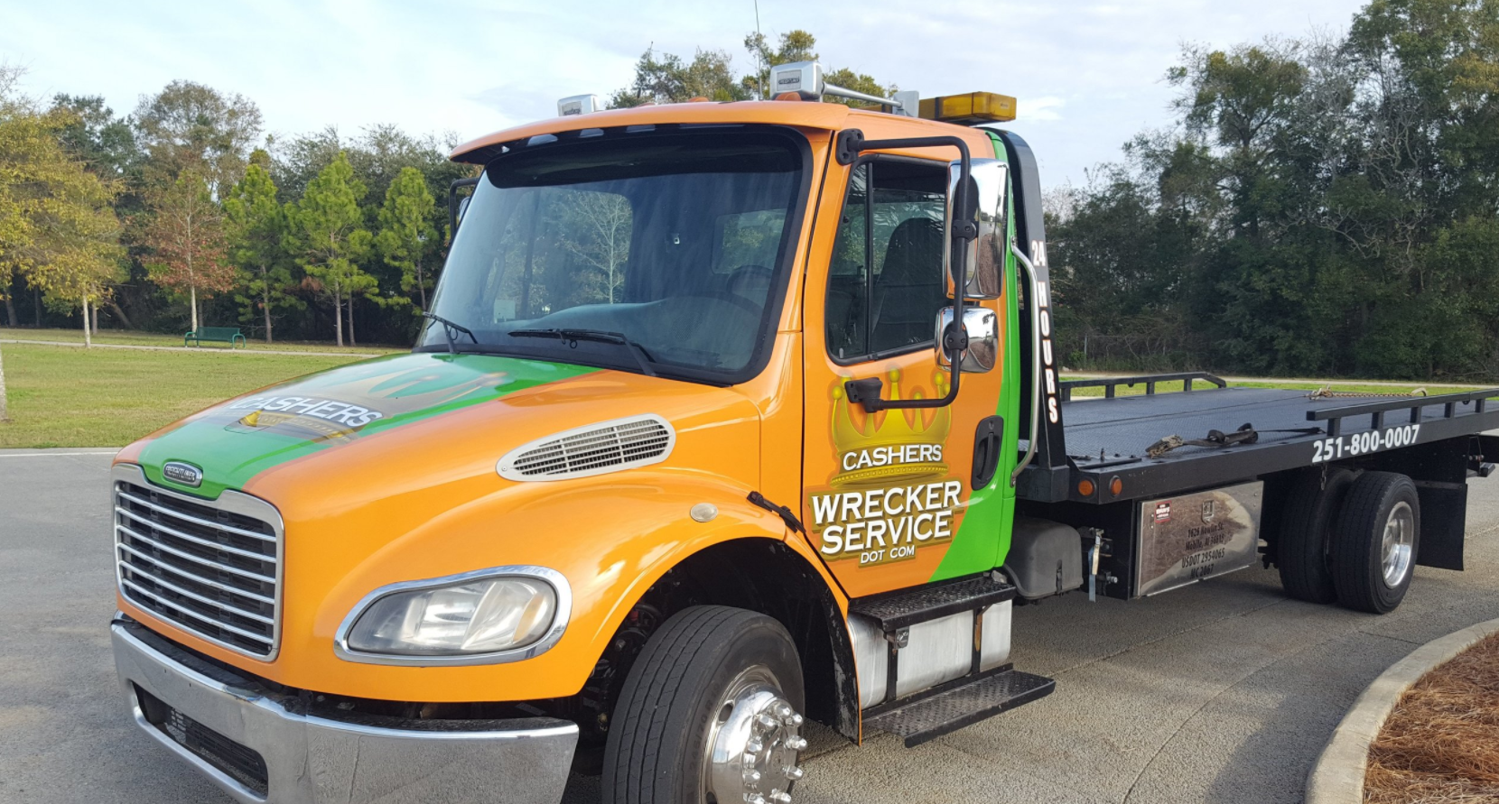 Orange and green flatbed tow truck parked on a road with trees in the background