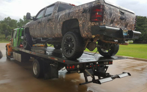 Camouflage pickup truck loaded on a black flatbed tow truck outdoors on a wet road