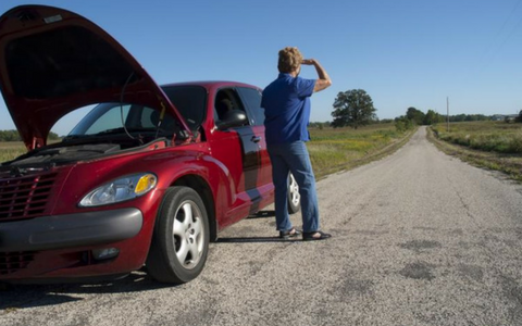 Red car with hood open on a rural road, while a person stands beside it using binoculars.