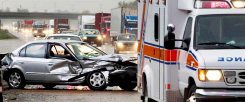 Picture of ambulance on side of road with busy traffic and car with extensive damage in background
