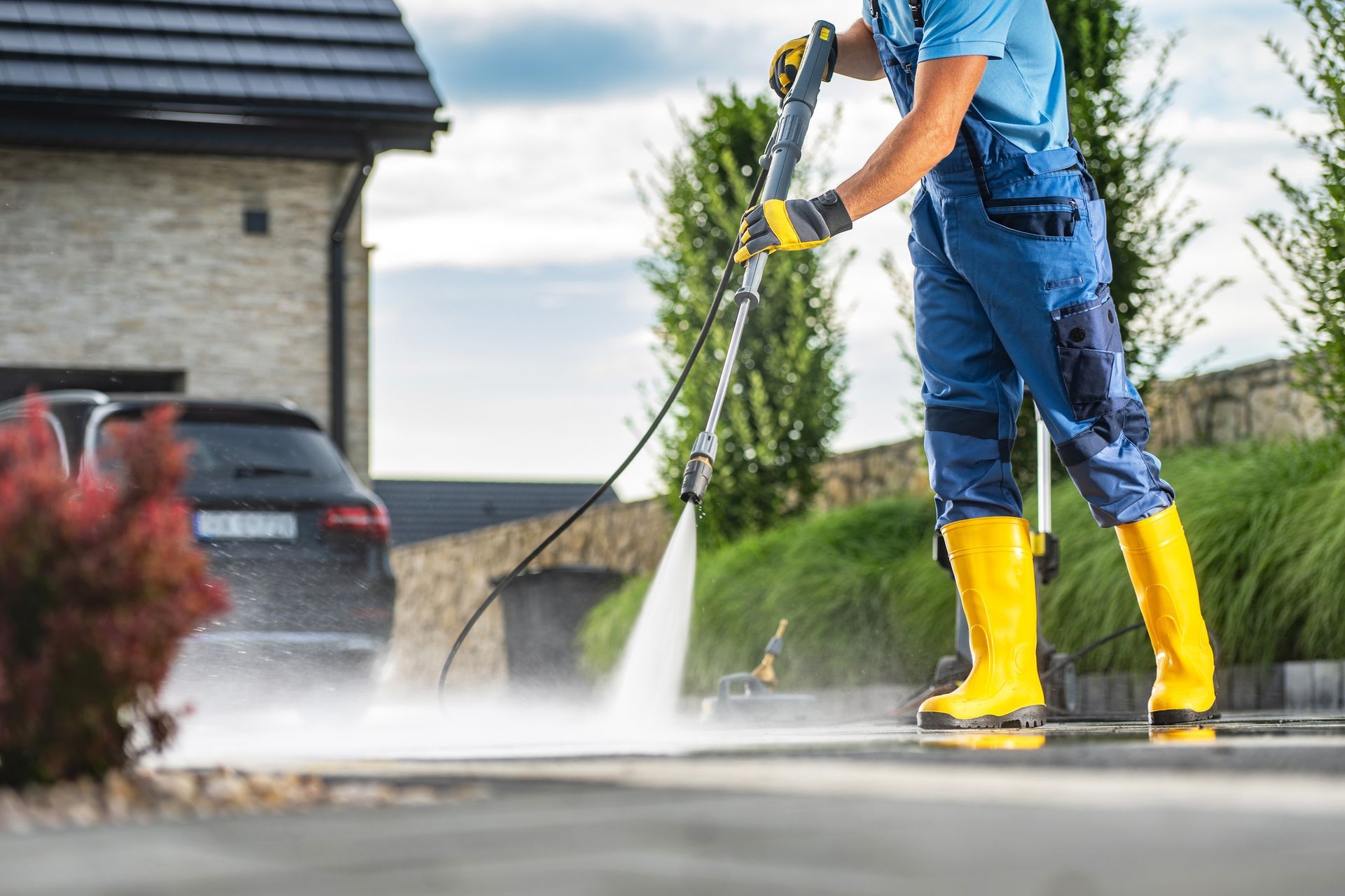 Cropped view of a worker wearing yellow boots, performing a driveway pressure washing service.