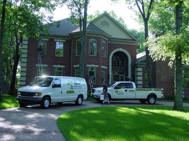 Residential pressure washing crew with service trucks at a two-story brick home driveway.