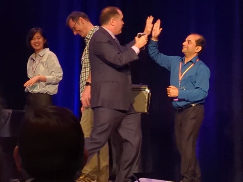 Magician David Martinez high-fives an audience volunteer on stage at a corporate event.
