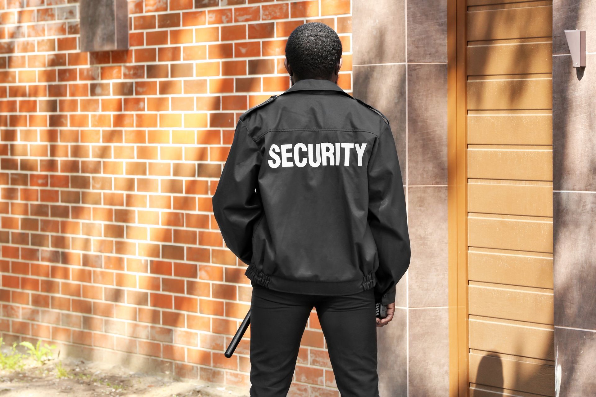 Security guard in black jacket standing on a city sidewalk near brick wall. Security guard in black jacket standing on a city sidewalk near brick wall.